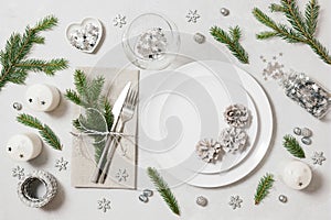 Festive table setting for Christmas dinner on white background. New Year serving with silver decor, fir branches and cones. View