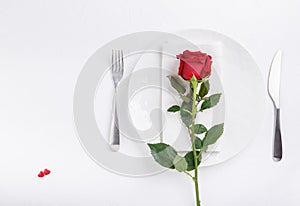 Festive table setting. Empty plate, knife, fork, napkin and red rose on white table. Top view, flat lay, copy space