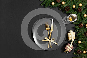 Festive table setting with golden cutlery, gifts and fir branches on a black background. Preparing for Christmas dinner. Copy