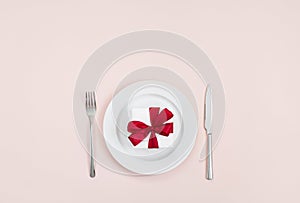 Festive table setting with a red gift in a plate on a pink background. Romantic or wedding dinner. Valentines day or mothers day