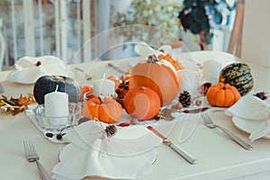 Festive table setting for Thanksgiving family home dinner. Fall composition with decorative pumpkins, nuts, cones