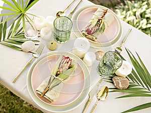 Festive table setting for two person in tropical style with flowers, candles and leaves.