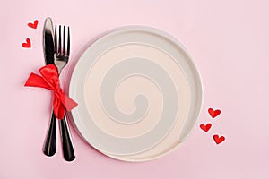 Festive table setting for Valentines Day with empty plate on pink table with red hearts