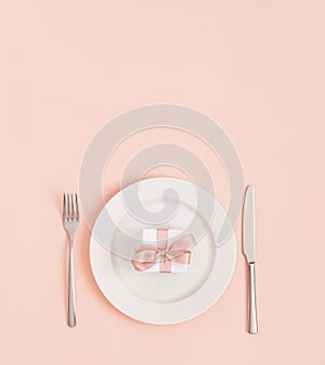 Festive table setting for Valentines Day, Mothers Day, Birthday or Christmas. Gift in a plate on a pastel pink background. Minimal