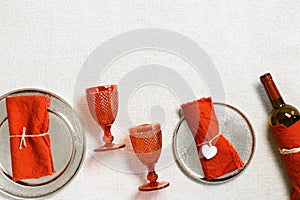 Festive table setting for Valentines Day with red glass colored wine glasses, bottle of red wine, linen napkins on table