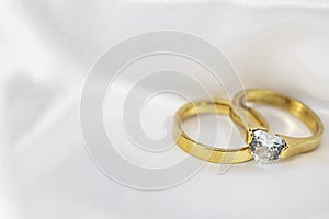 Festive wedding background with two gold rings with diamond on white satin material. Copy space.