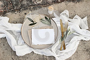 Festive wedding summer table setting. Golden cutlery, olive branch, glass of wine and envelope on porcelain dinner plate