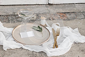 Festive wedding summer table setting. Golden cutlery, olive branch, glass of wine and silk ribbon on dinner plate