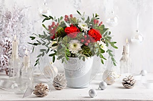 Festive winter flower arrangement with red roses, white chrysanthemum and berries in vase on table. Christmas flower composition f