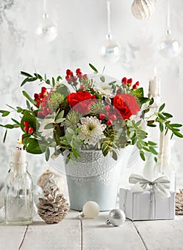 Festive winter flower arrangement with red roses, white chrysanthemum and berries in vase on table decorated for holiday. photo