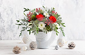 Festive winter flower arrangement in vase  and Christmas baubles on table.