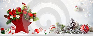 Festive winter flower arrangement in vase of red star shape and Christmas baubles on table. Christmas flower composition for