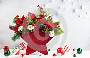 Festive winter flower arrangement in vase of red star shape and Christmas decorations on table