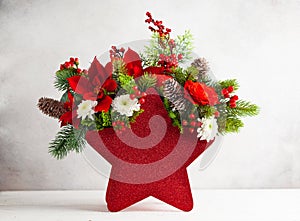 Festive winter flower arrangement in vase of red star shape. Christmas flower composition for holiday