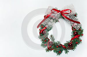 Festive wreath on the door of spruce branches, decorated with red berries, ribbons, balls and a beautiful lace bow on a white bac