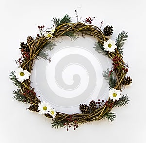 Festive wreath of vines decorated with berries, fir branches, daisy flowers and cones. Flat lay, top view