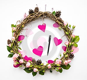 Festive wreath of vines with decorative roses and pink paper hearts. Flat lay, top view