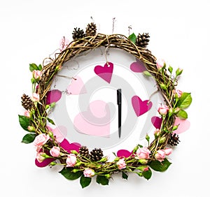 Festive wreath of vines with decorative roses and pink paper hearts. Flat lay, top view