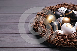 Festively decorated Easter eggs and vine wreath on grey wooden table, closeup. Space for text