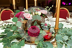 Festively decorated round banquet table in the restaurant. Fresh flowers are golden candles and garnet and red chairs. expensively