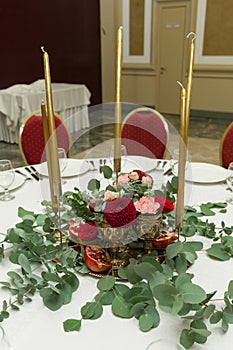 Festively decorated round banquet table in the restaurant. Fresh flowers are golden candles and garnet and red chairs. expensively