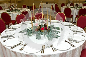 Festively decorated round banquet table in the restaurant. Fresh flowers are golden candles and red chairs. expensively rich