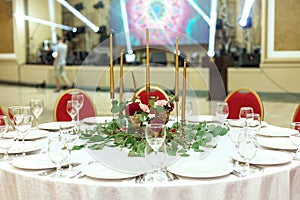 Festively decorated round banquet table in the restaurant. Fresh flowers are golden candles and red chairs. expensively rich