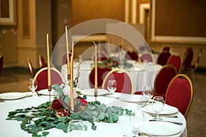 Festively decorated round banquet table in the restaurant. Fresh flowers are golden candles and red chairs. expensively rich