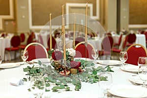 Festively decorated round banquet table in the restaurant. Fresh flowers are golden candles and red chairs. expensively rich