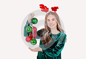 Festively dressed cute girl wearing reindeer antlers holding Christmas decorations on isolated white background