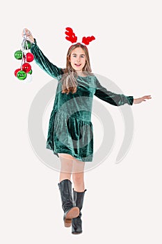 Festively dressed cute girl wearing reindeer antlers holding Christmas decorations on isolated white background