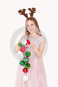 Festively dressed cute girl wearing reindeer antlers holding Christmas decorations on isolated white background