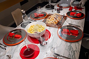 Festively set table. Silver plates on red placemats on marble top. Filet Wellington, potato salad, Cumberland sauce