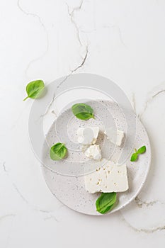 Feta cheese with basil leaves on plate and white background