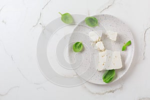 Feta cheese with basil leaves on plate and white background