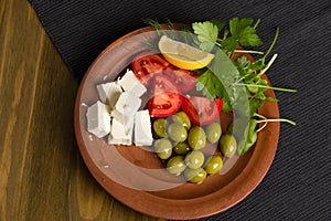 Feta cheese, tomatoes, olives and herbs in a clay plate