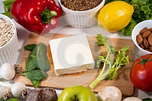 Feta cheese on a wooden board, as well as red bell pepper, tomato, lettuce, mushrooms, lemon on the table. Food products