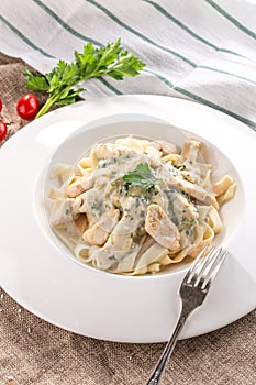 Fettuccine pasta with chicken and cheese sauce on white plate on tablecloth