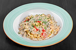 Fettuccine pasta with chicken meat, tomato, mushrooms, cheese sauce and greens on plate