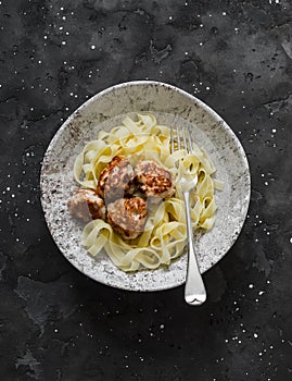 Fettuccine pasta with chicken teriyaki meatballs on a dark background, top view