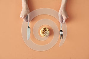 Fettuccine pasta, fork and knife in hands  on beige background, minimalistic photography for food blog or ad