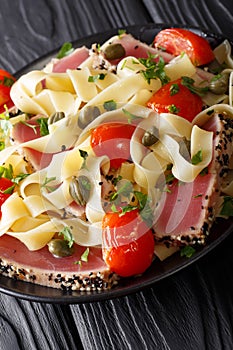 Fettuccine pasta with fried tuna steak, tomatoes and capers close-up on a plate. vertical