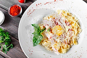 Fettuccine pasta with meat, ham, egg, parmesan cheese, basil and cream sauce on plate