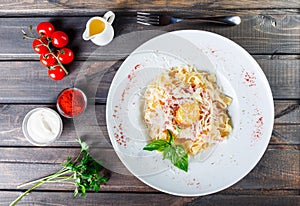 Fettuccine pasta with meat, ham, egg, parmesan cheese, basil and cream sauce on plate on dark wooden background