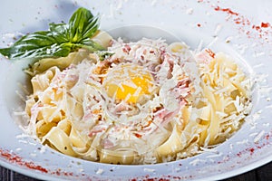 Fettuccine pasta with meat, ham, egg, parmesan cheese, basil and cream sauce on plate on dark wooden background