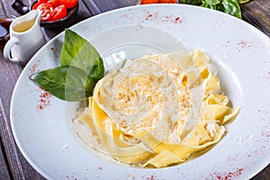 Fettuccine pasta with parmesan cheese, basil and cream sauce on dark wooden background