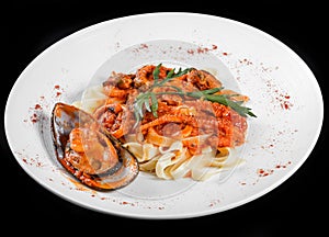 Fettuccine pasta with seafood, mussels, octopus, oysters, tomato sauce and herbs, in bowl isolated on black background