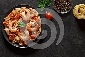 Fettuccine pasta, shrimp, tomatoes, spices, parsley - cooked Italian dish with ingredients, on dark background, top view, space to