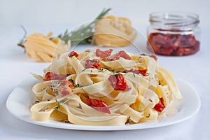 Fettuccine pasta with sun-dried tomatoes and fresh herbs are lying on a white plate. Isolated object