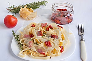 Fettuccine pasta with sun-dried tomatoes is lying on a white plate
